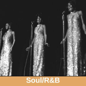 Black and white photo of the three women of the Supremes - three black women in silver beaded gowns singing at microphones on stands